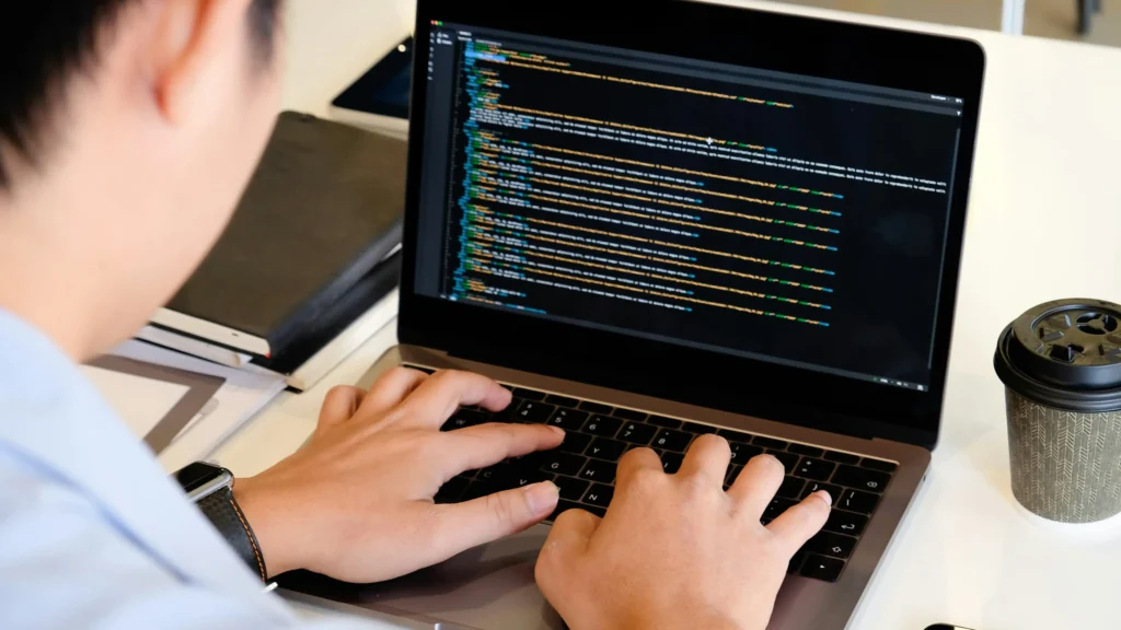 Un développeur qui code installé à son ordinateur portable.